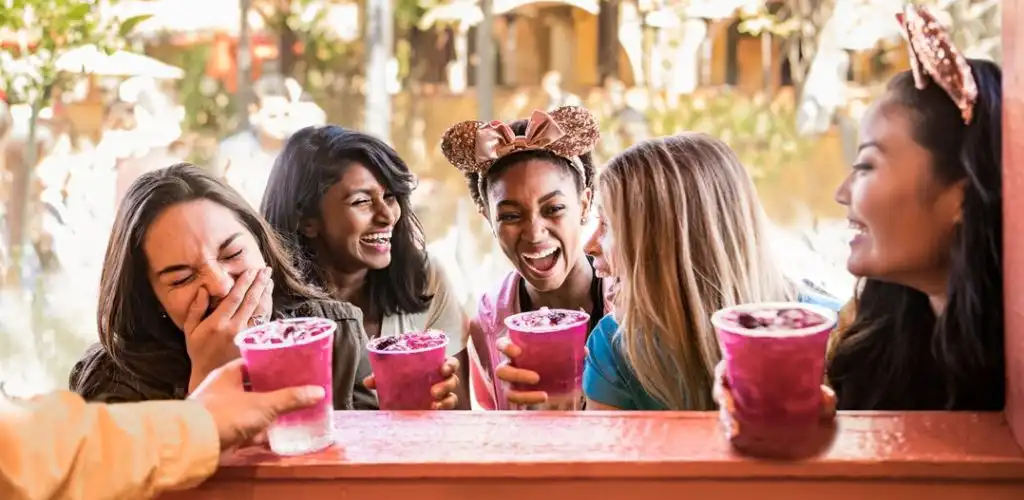 Group of women happily enjoying colorful drinks outdoors at a cafe window during daytime