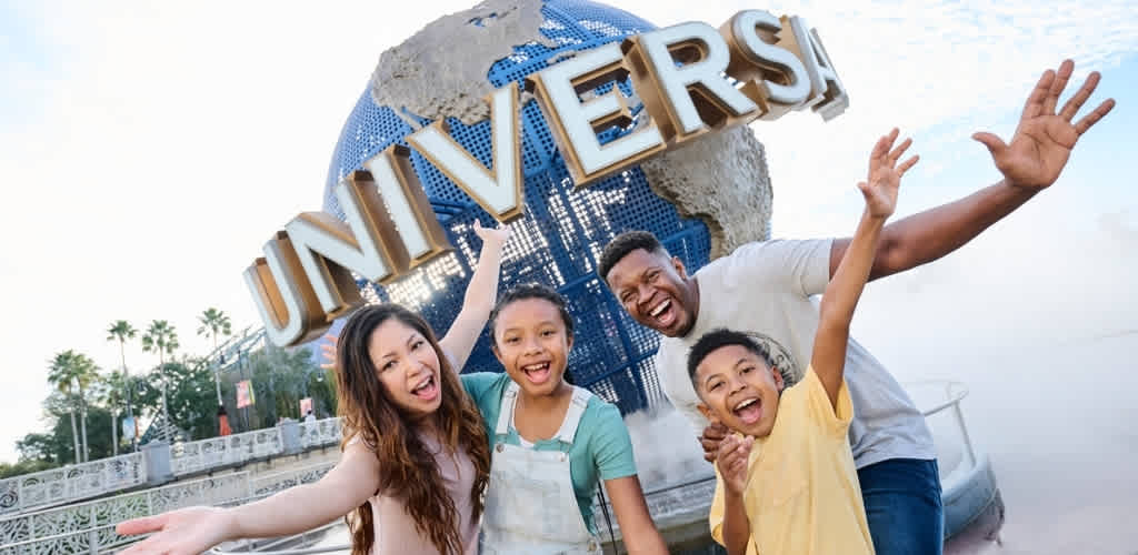 Group of people smiling and waving in front of a globe with the word UNIVERSE on it at an amusement park