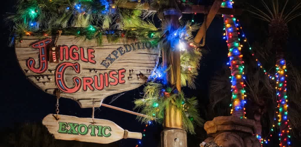 A wooden sign for Jingle Cruise with colorful lights and festive greenery decorations at night
