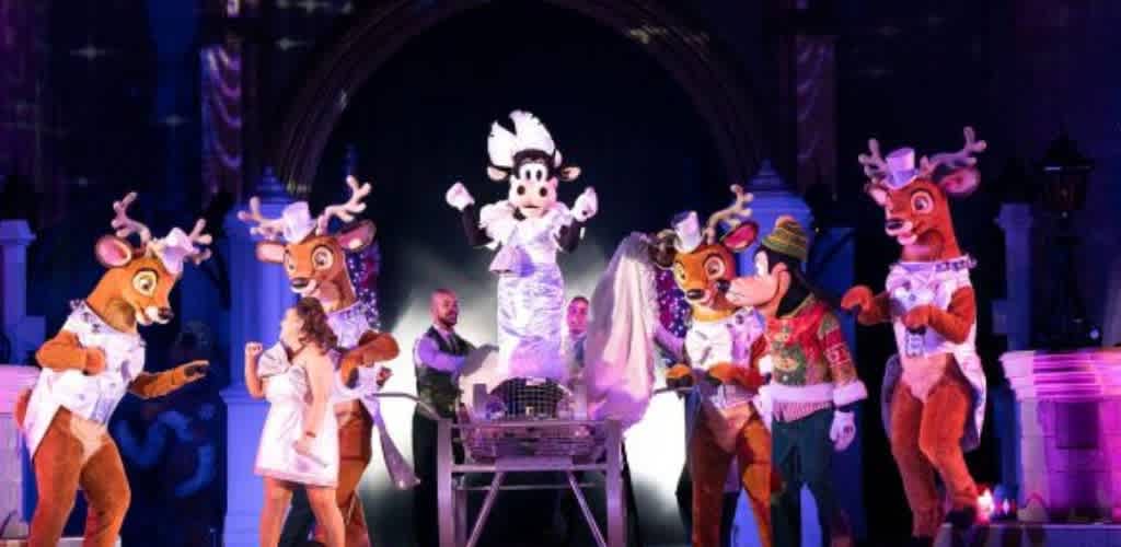 Costumed characters performing on stage with a backdrop of purple and blue lights, including a central character in white and others dressed as animals and a person in a fedora.