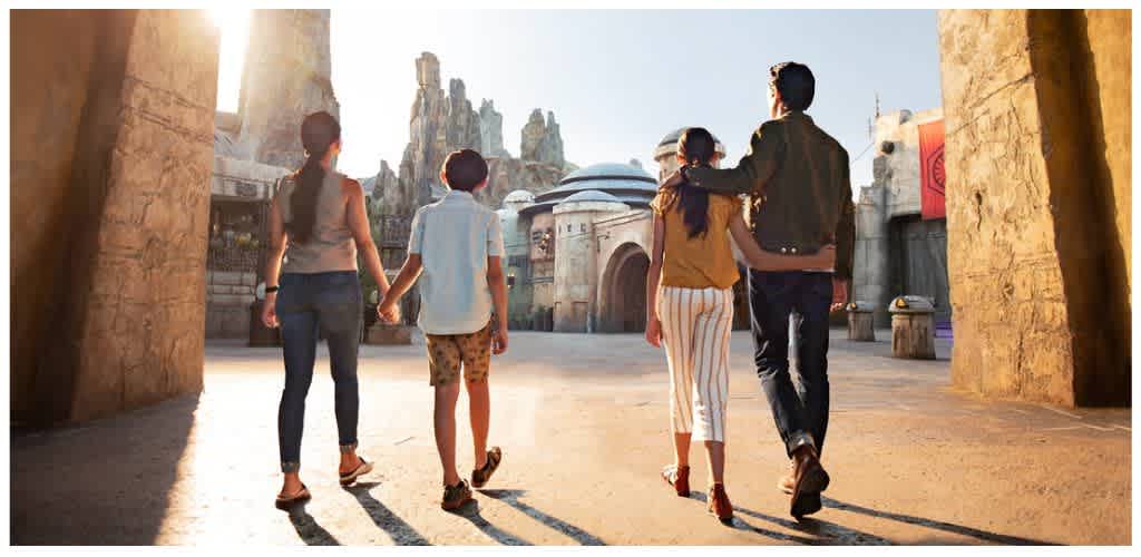 Group of people walking through a themed outdoor area with large structures and a bright sky