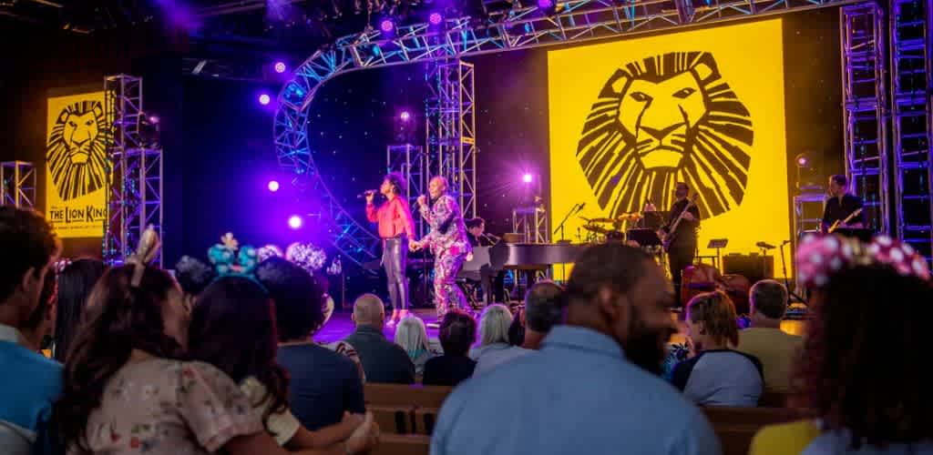 A live musical performance on stage with Lions King themed visuals and audience watching attentively