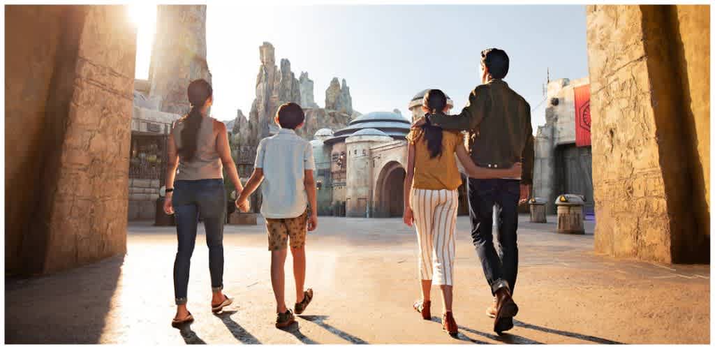 Four people walk together in a themed outdoor environment with futuristic architecture and rocky formations in the background.