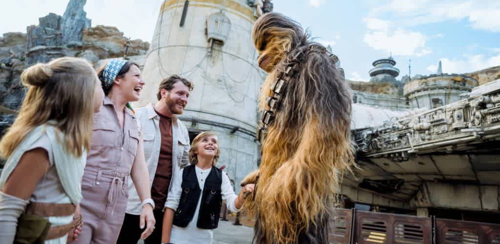 Group of people smiling and interacting with a large Chewbacca character from Star Wars outside in a themed environment