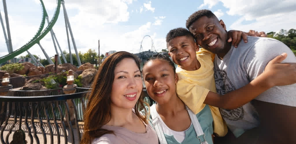 A happy diverse family enjoying a day at an amusement park with rides and a bright blue sky in the background