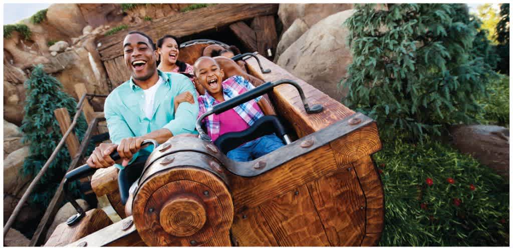 A group of people enjoying a wooden roller coaster ride with smiles and laughter in an outdoor theme park setting.