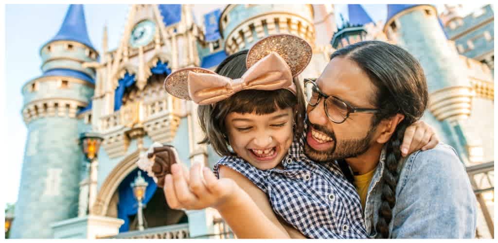 A father and daughter smiling happily in front of a Disney castle at Disneyland with the daughter wearing Minnie Mouse ears.