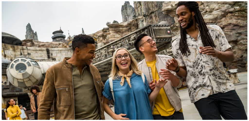 Group of diverse friends smiling and talking outdoors at a Star Wars themed attraction with spaceship structures in the background