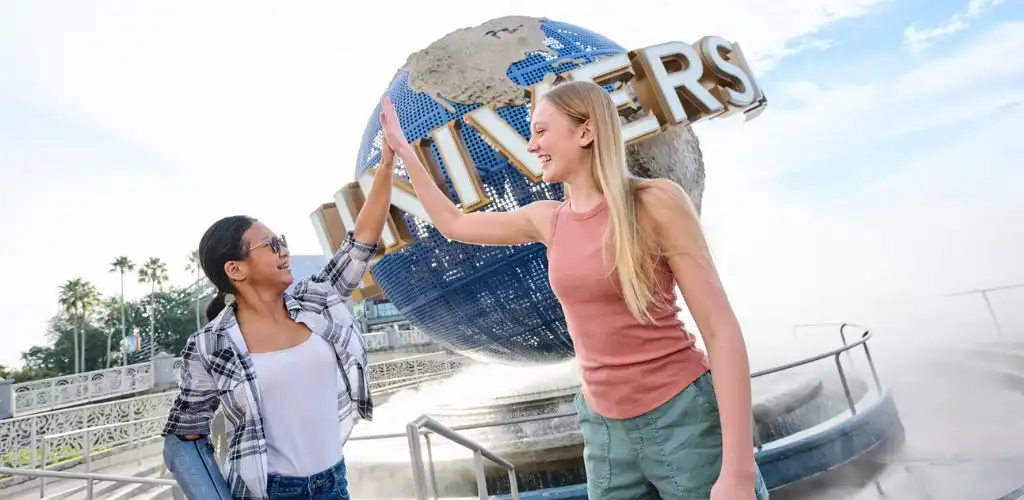 Two women giving a high five in front of a globe-shaped Universal Studios sign outside.