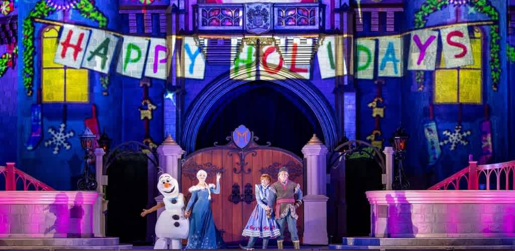 Colorful castle stage with characters from Frozen celebrating a happy holiday with a vibrant banner overhead that reads Happy Holidays