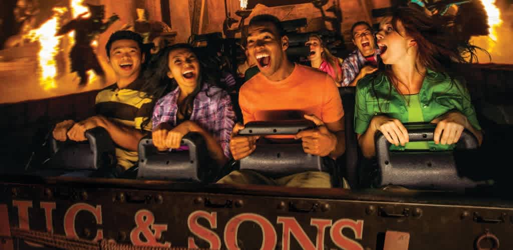 A group of excited people enjoying a thrilling amusement park ride at night with bright lights and laughter.