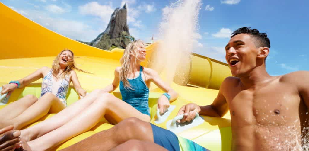 Three young people enjoying a ride on a yellow water slide outdoors on a sunny day
