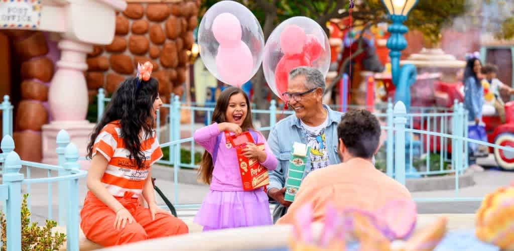 Family smiling and enjoying time outdoors at a colorful amusement park with balloons and rides in the background