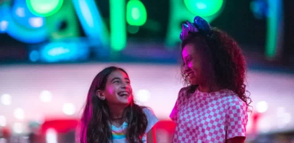 Two women smiling and laughing together at night illuminated by colorful neon lights
