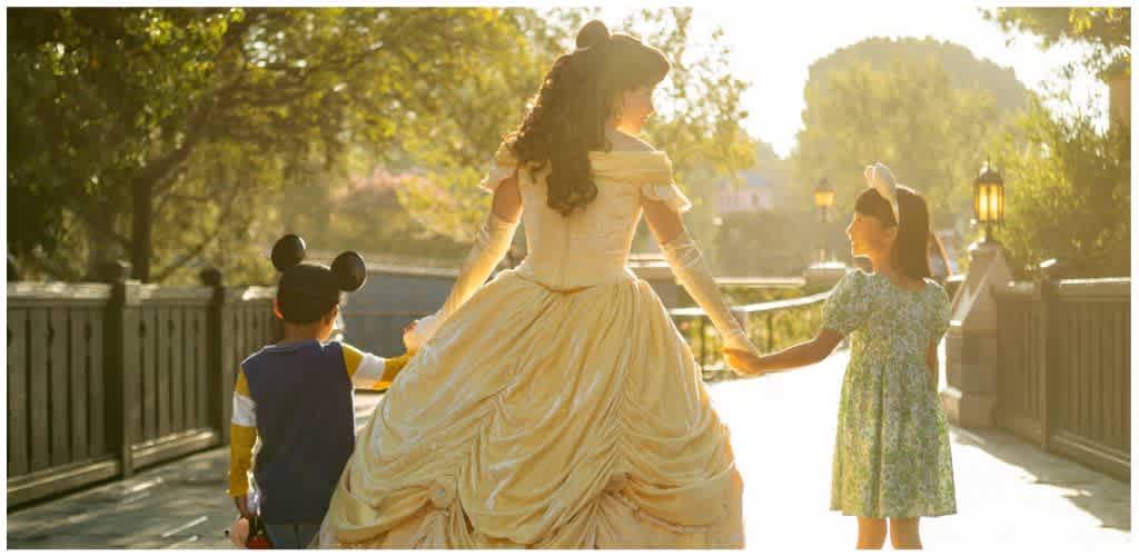 Woman in princess gown holding hands with two children on a bridge during sunset