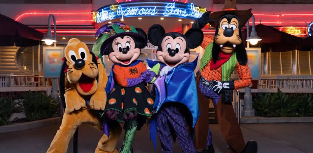 Costumed characters of Pluto Minnie Mouse Mickey Mouse and Goofy smiling and posing together outside at night