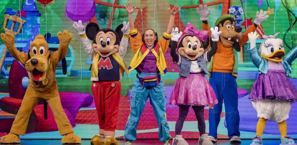 Costumed characters including Mickey Mouse, Minnie Mouse, Pluto, and Daisy Duck performing on a colorful stage for children.