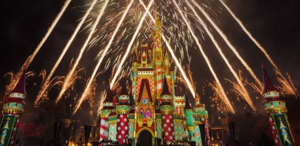 A colorful Disney castle illuminated with festive lights and fireworks lighting up the night sky.