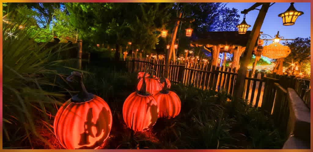 Colorful illuminated pumpkins with Jack-O-Lantern faces at an outdoor themed park at dusk