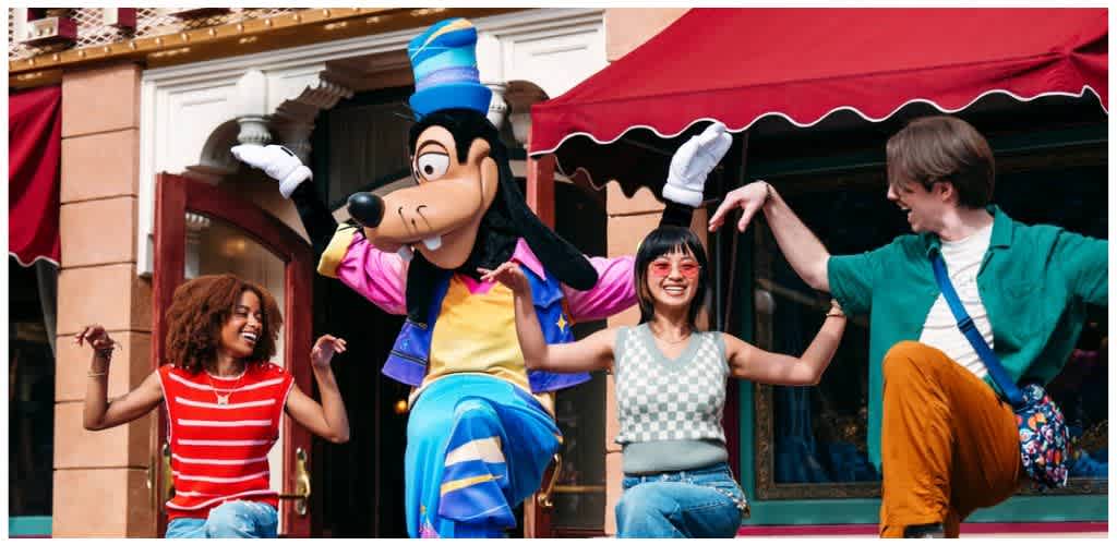 People dancing with a large Goofy character outside a building at a theme park