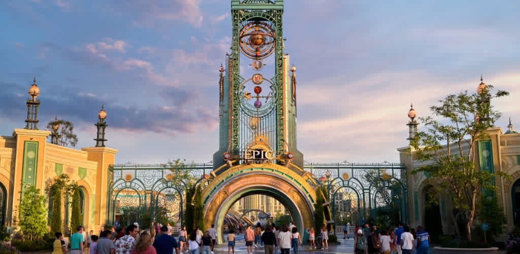 The entrance to Epic Universe theme park features a large decorative arch with colorful details and a tall green structure with an eye motif at the top.