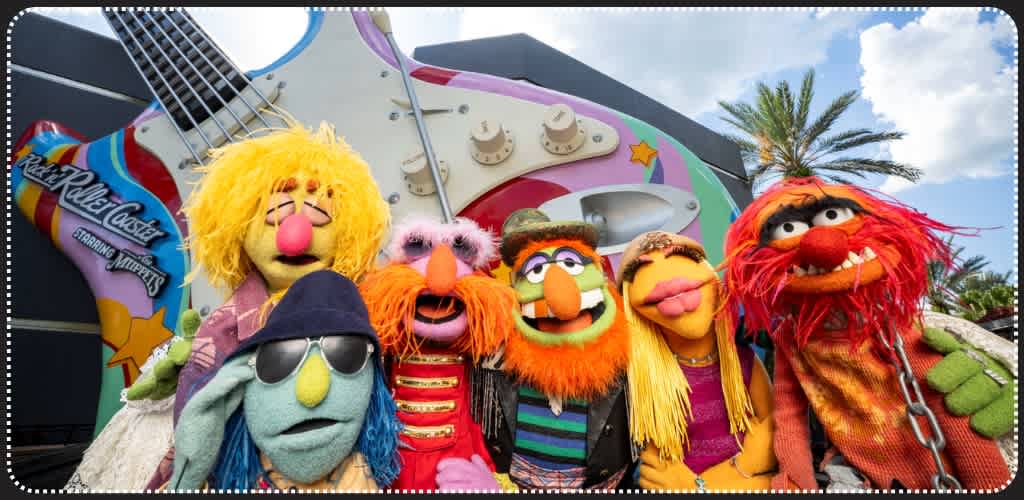 Group of colorful Muppets characters standing outdoors in front of a giant guitar sculpture with a cloudy sky and palm trees.
