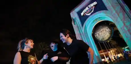 Three people are smiling and talking outside a themed event venue at night with the words Universal Studios here.