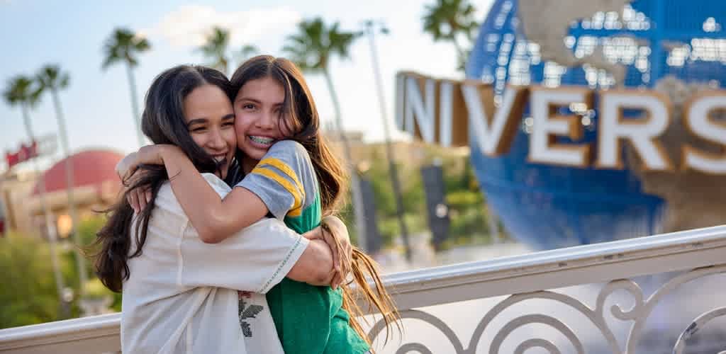 Two children hugging each other in front of a Universal Studios sign during daytime.