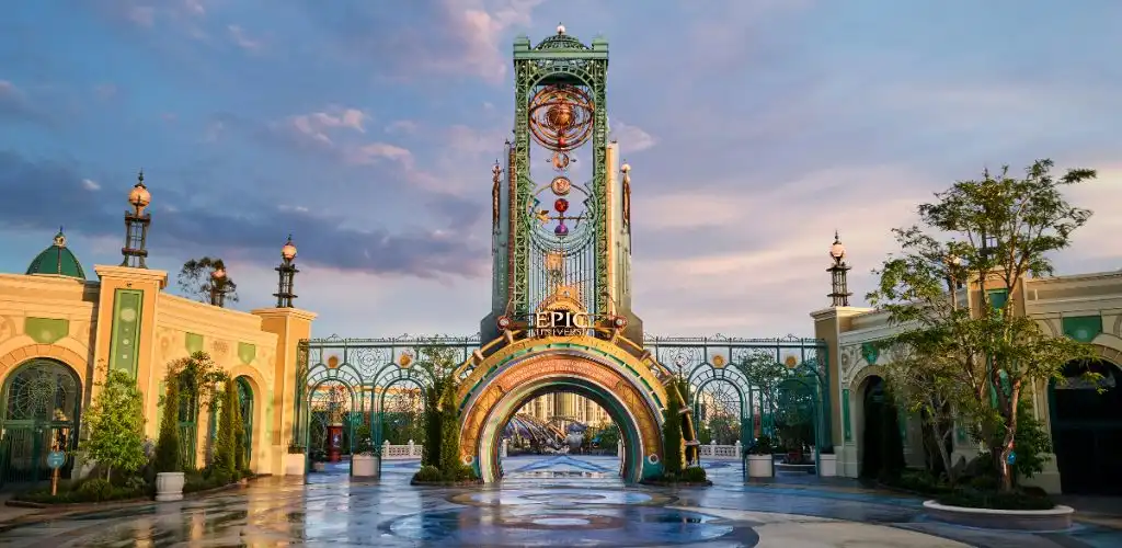 Entrance to an amusement park with colorful decorative elements and a tall central archway during sunset.