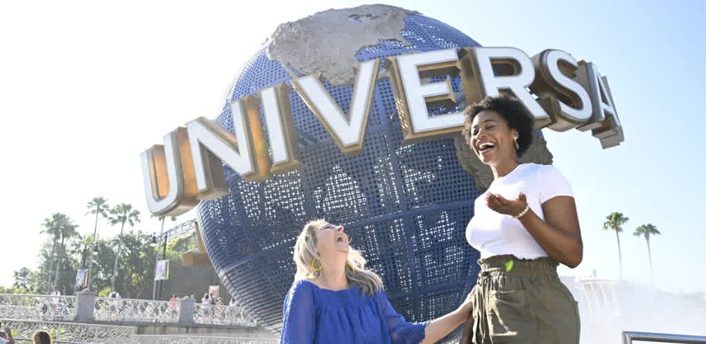 Two women smiling and laughing in front of a large globe with the Universal Pictures logo at Universal Studios theme park