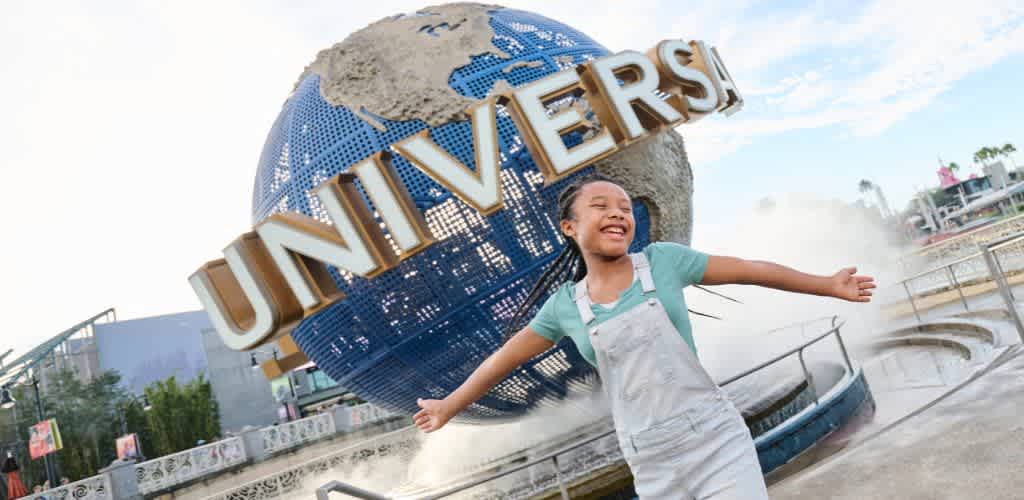 A smiling girl stands with outstretched arms in front of the Universal Studios globe fountain outside the theme park.