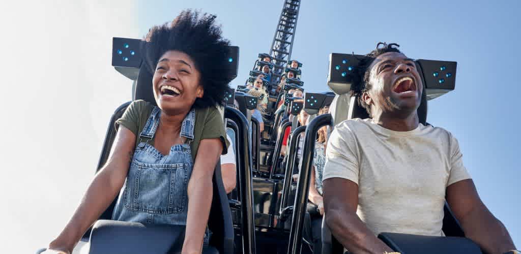 Two people on a roller coaster experiencing excitement and joy during the ride with blue sky in the background