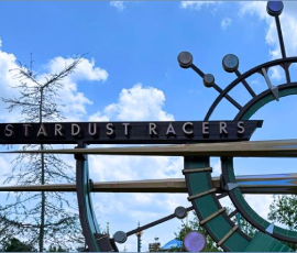 A metal sign reading Stardust Racers with a large circular decorative element and starburst design against a blue sky with clouds.