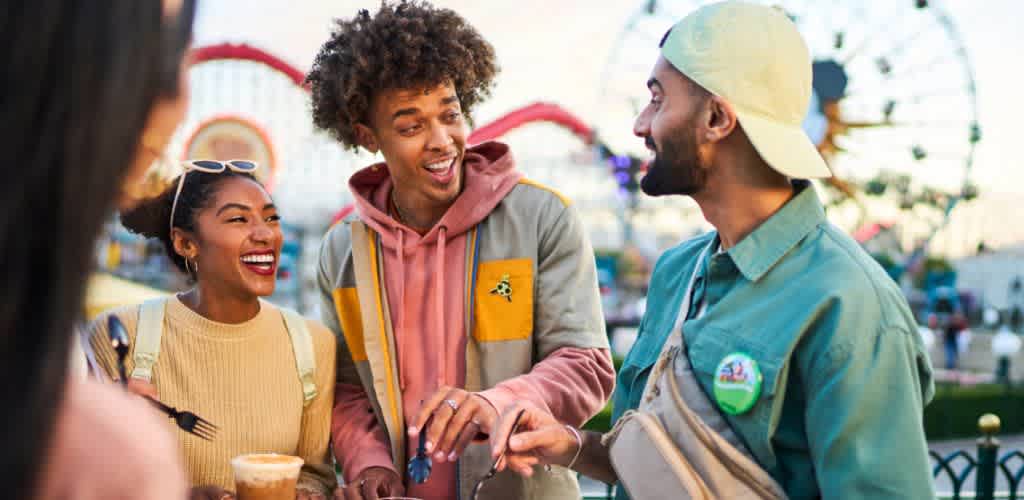 Four diverse friends are enjoying conversation outdoors at an amusement park during daytime.