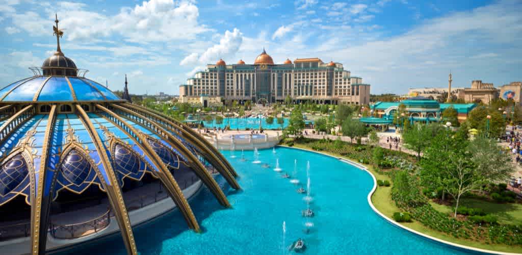 A large ornate building with a dome and a pond with fountains, surrounded by greenery and other structures under a partly cloudy sky