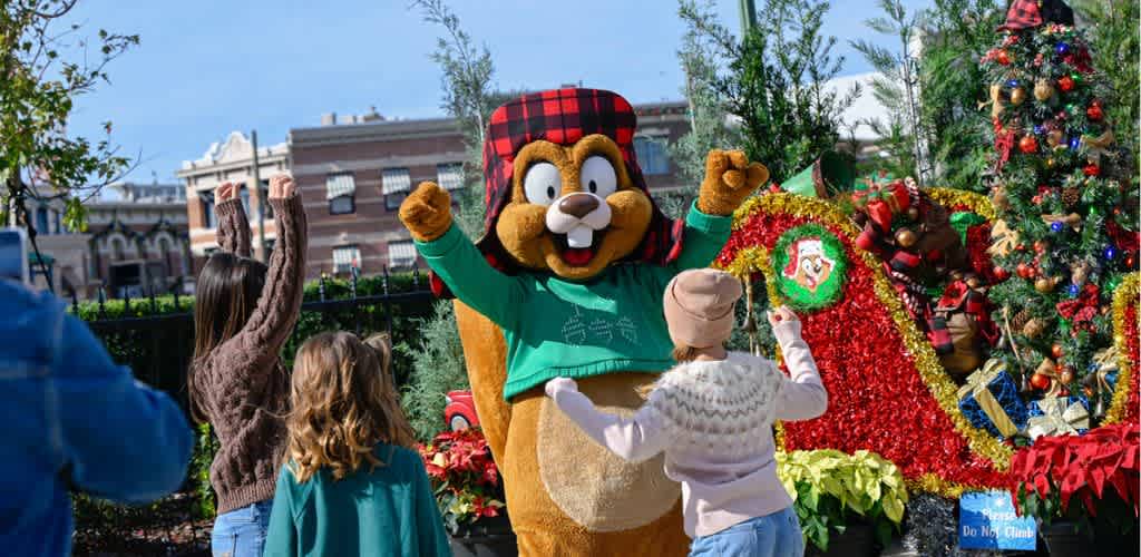 Children celebrating outdoors with a festive holiday character in front of decorated Christmas trees and poinsettias.