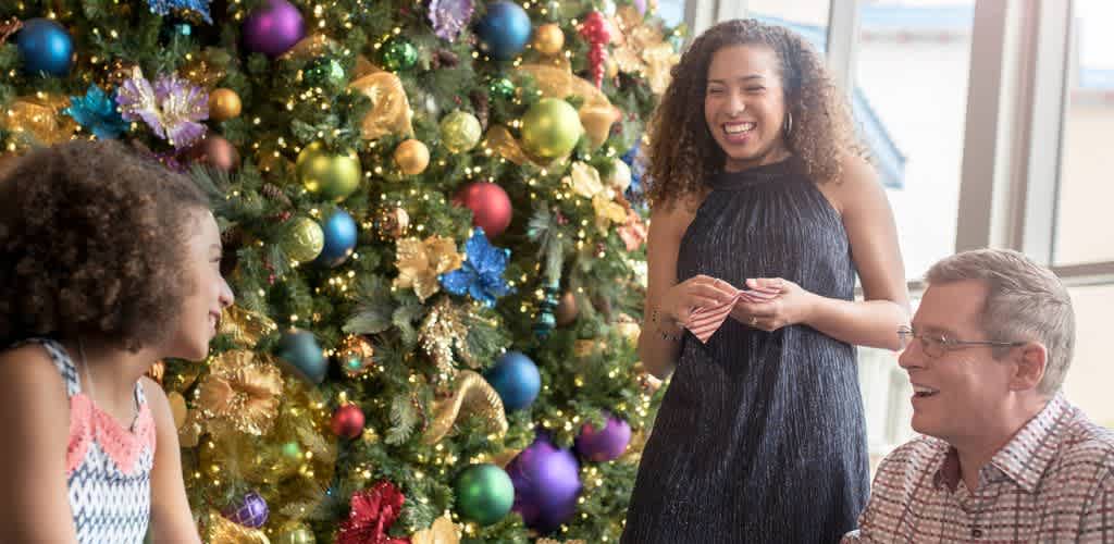 Three people smiling and talking near a decorated Christmas tree indoors during the holiday season