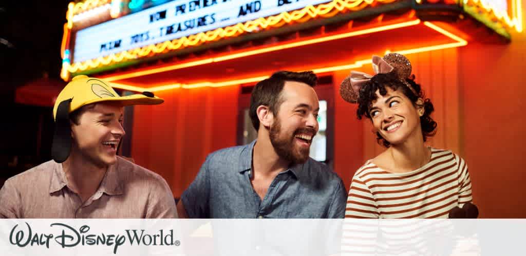 Three friends laughing and enjoying their time at Disney’s Hollywood Studios After Hours, with glowing neon lights in the background creating a vibrant night settin