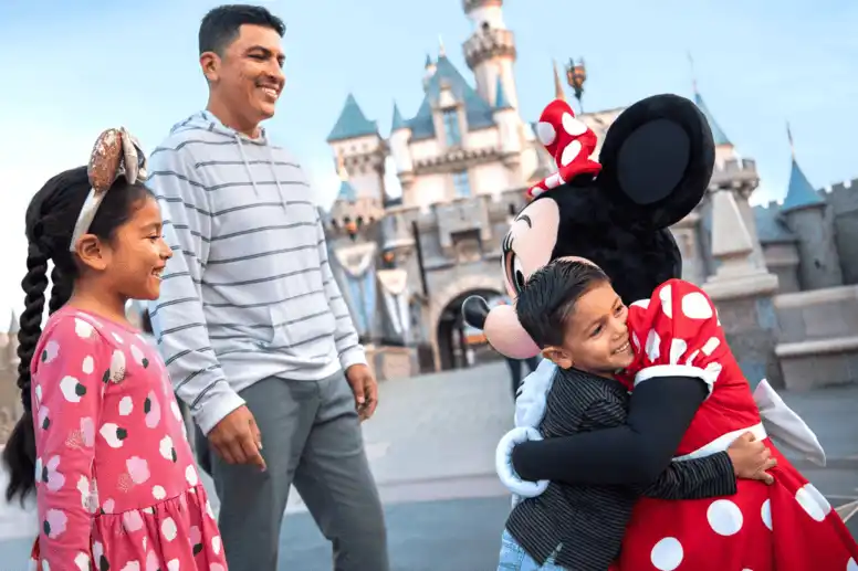 A smiling family meeting Minnie Mouse in front of Sleeping Beauty Castle at Disneyland Resort, creating magical memories.