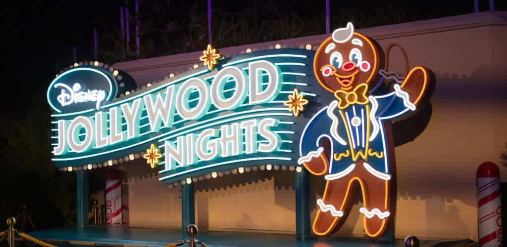 Brightly lit Disney Jollywood Nights sign with a smiling clown character waving on a dark night background.