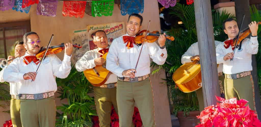 Group of musicians playing guitars and violins outdoors with colorful decorations and green plants.