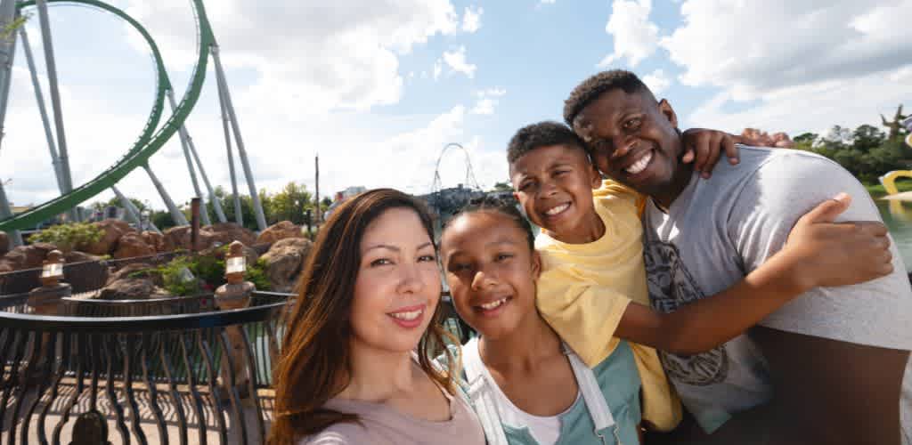 Happy family taking a selfie at Universal’s Islands of Adventure, with a thrilling roller coaster twisting in the background on a bright, sunny day.
    