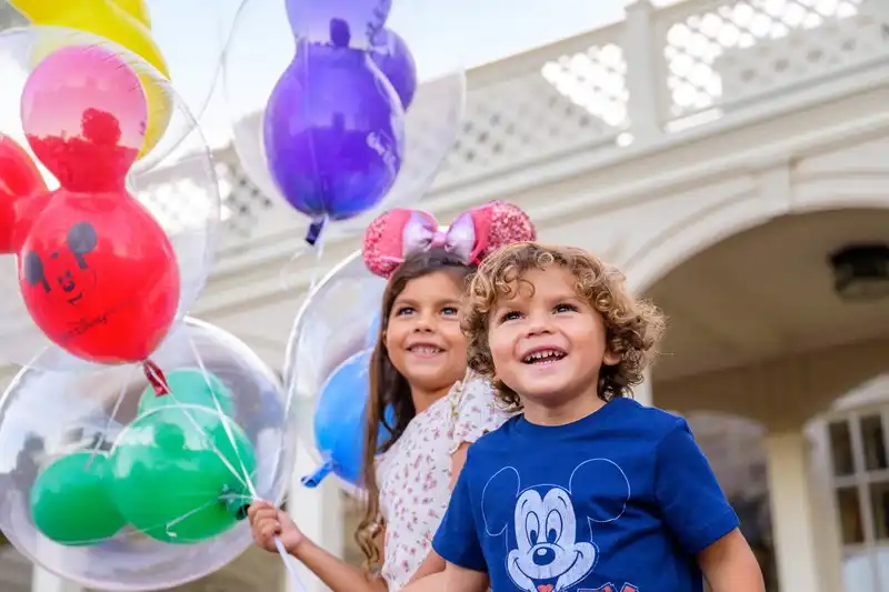 Smiling children holding colorful Mickey balloons at Walt Disney World, capturing the joy and wonder of a magical day at the parks.