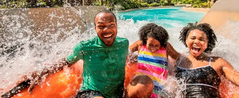 A joyful family makes a big splash on a thrilling water ride at Disney’s Typhoon Lagoon, surrounded by tropical palm trees and bright sunshine.