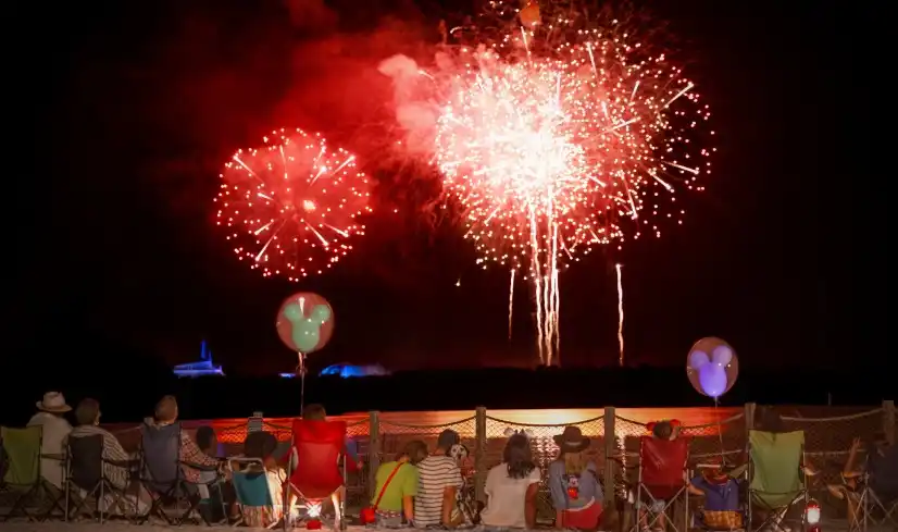 Families relax in cozy chairs along the waterfront, watching a breathtaking Disney fireworks show light up the night sky.
