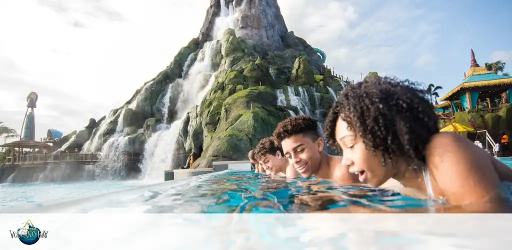 Friends relaxing in the infinity pool at Universal’s Volcano Bay, enjoying the tropical atmosphere with the stunning Krakatau volcano and cascading waterfalls in the background.