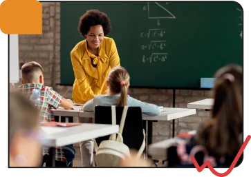 A smiling female teacher in a yellow jacket engaging young students in a classroom with a chalkboard background and educational materials.
