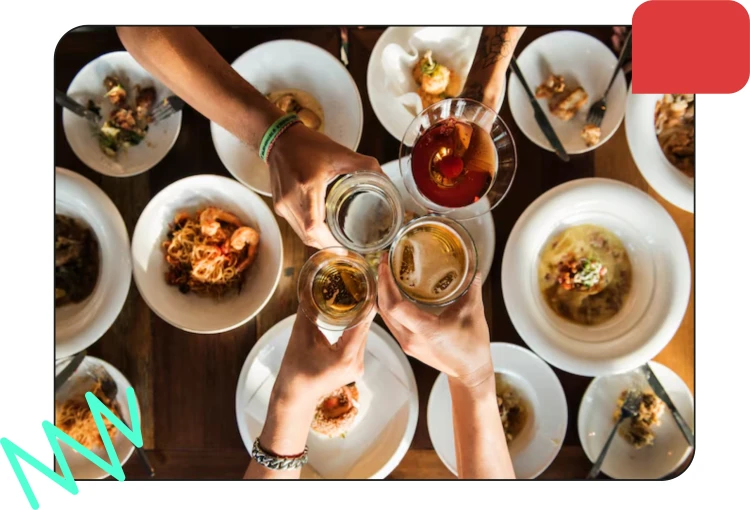 People clinking glasses of drinks above plates of food at a table in a restaurant.