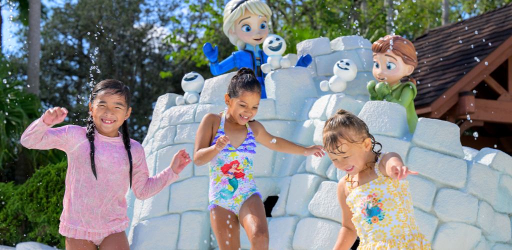 Children playing on a colorful water park with animated snowman characters and a castle structure outdoors on a sunny day