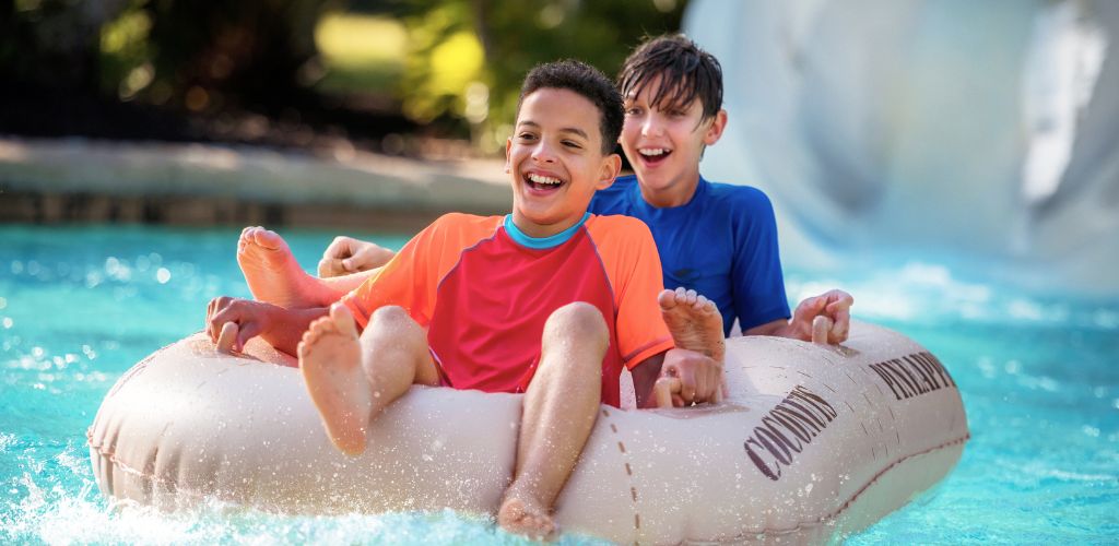 Two children are riding on an inflatable raft in a swimming pool, smiling and having fun during a sunny day.